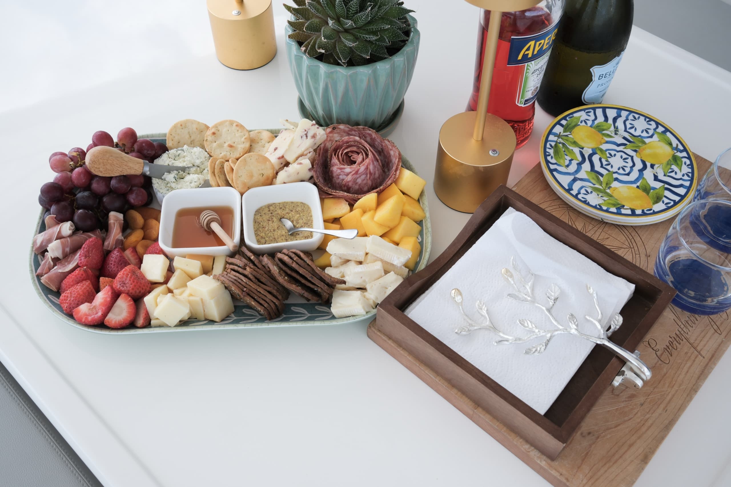 A charcuterie board and place settings with a bottle of Aperol and prosecco in the background.